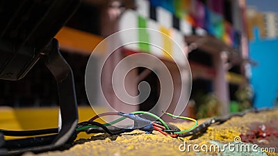 A bunch of colorful wires in the foreground over a yellow wall with a colorful building in the background Stock Photo