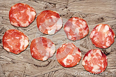 Bunch of Eight Pork Salami Slices Set On Rustic Wooden Chipboard Rough Grunge Surface Stock Photo