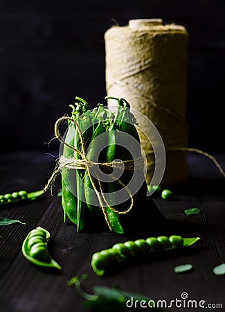 Bunch of fresh mature pods of green peas tied with a rope on black wooden background. Bio healthy food. Green peas, pods. Stock Photo