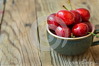 Bunch of fresh ripe colorful glossy sweet cherries in ceramic tea cup on wood background, minimalist, copy space for text Stock Photo