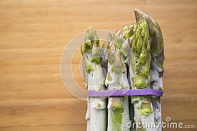 Bunch of frozen wild asparagus tied with rubber tape from ecological agricuture over wooden background Stock Photo