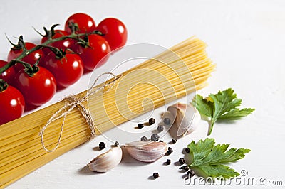 Bunch of raw spaghetti, cherry tomatoes, peppers, garlic cloves and parsley leaves on a white wooden background. Close-up Stock Photo