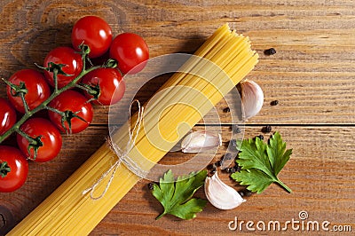 Bunch of raw spaghetti tied with rope, tomatoes cherry, slices of garlic, parsley leaves and pepper on brown wooden background. Stock Photo