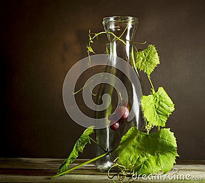 Bunch of ripe grapes in an old bottle entwined leaves. Stock Photo