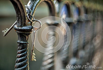 A bunch of two metal old vintage door keys hanging on a cast-iron fence of artistic casting in a park with a blurred background Stock Photo