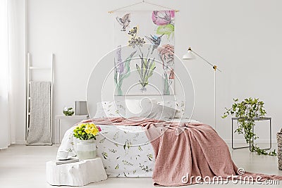 A bunch of yellow fresh cut flowers in a bright bedroom interior with a bed dressed in white linen and peach blanket. Fabric on th Stock Photo