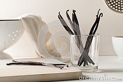 Bundle of dried bourbon vanilla beans or pods on wooden cutting board and in glass on white kitchen background Stock Photo