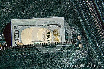 A bundle of hundred-dollar bills sticks out of the pocket of a leather jacket of green color. Shooting close-up Stock Photo