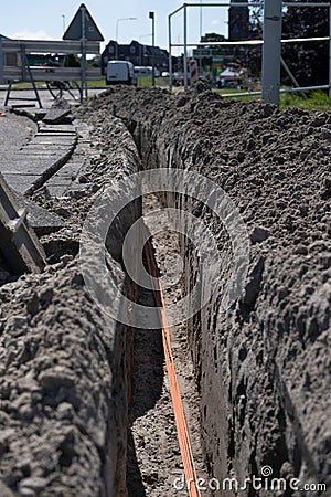 Bundle of orange fiber optic cables lie in a dug trench in the ground in a street Stock Photo