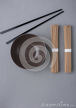 Bundles of Soba Noodles Dark Empty Bowl Black Bamboo Chopsticks on Grey Background. Japanese Chinese Asian Cuisine. Menu Poster Stock Photo