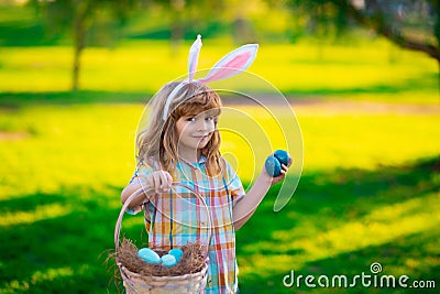 Bunny child with hunting easter eggs. Easter bunny children. Kids boy in bunny ears hunting easter eggs in park outdoor. Stock Photo