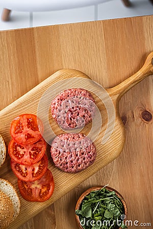 Buns, raw beef cutlets, tomatoes and herbs for burgers cooking Stock Photo