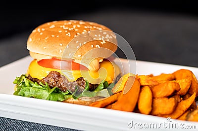 Burger meal on plate. Delicious hamburger with juicy beef, melting cheddar cheese served with crispy sweet potato fries. Stock Photo