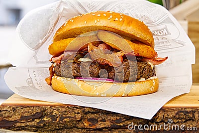 Burger in paper packaging on a wooden beard. delicious burger on a wooden serving board. Stock Photo