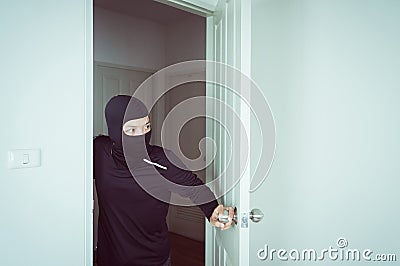 Burglar in black mask looking and open the door and stealing something from home Stock Photo