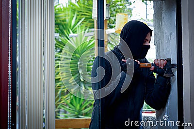 Burglar with crowbar trying break the window to enter the house Stock Photo