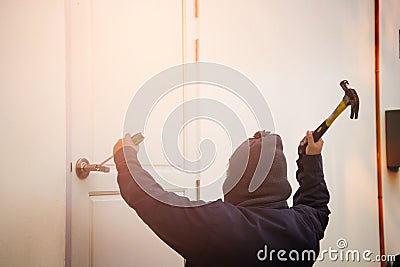 Burglar trying to break into a house with a hammer and Stock Photo