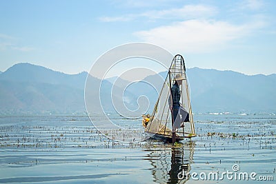 Burmese fisherman on bamboo boat catching fish in traditional way with handmade net. Inle lake, Myanmar Burma Editorial Stock Photo