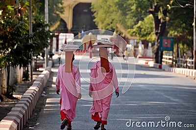 Burmese nuns women put holding tray on head walking on street at beside road front of ancient ruins building of Mandalay Palace go Editorial Stock Photo