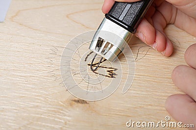 Burn out a drawing on a wooden board with an electric device with a scorcher Stock Photo
