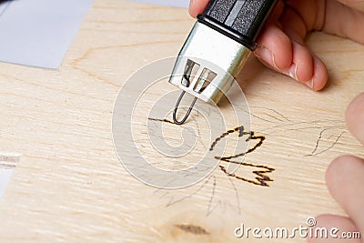 Burn out a drawing on a wooden board with an electric device with a scorcher Stock Photo