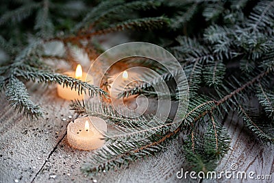 Burning candle and Christmas decoration over snow with pine branches on white wooden background Stock Photo