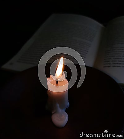 a burning candle illuminates the reading book Stock Photo