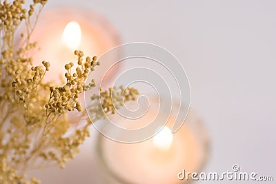 Burning candles in crystal cups on white background, delicate small beige spring flowers, top view, defocused Stock Photo