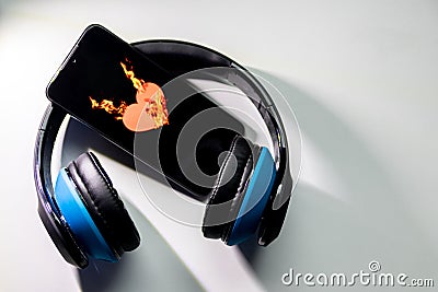 Burning heart symbol with burning flames on a black smartphone screen and blue over ear headphones and copy space Stock Photo