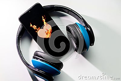 Burning heart symbol with burning flames on a black smartphone screen and blue over ear headphones and copy space Stock Photo