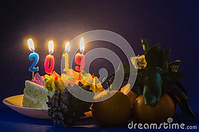 Burning holiday candles on cake on a white saucer and tangerines with a lump. New Year 2019 Stock Photo