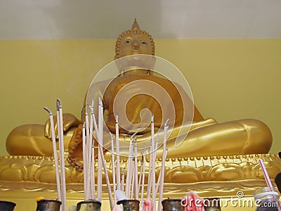 Burning incense sticks in front of a gold Buddha statue with waving smoking Stock Photo