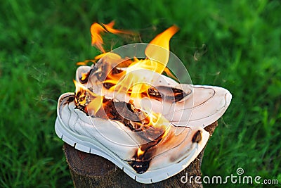 Burning leather sports shoes. Sneakers or gym shoes on fire stand on the Stump. Stock Photo