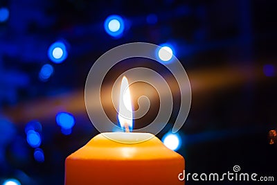 A burning orange candle on a dark background with blue lights - a Christmas New Year`s eve divination mystic esoteric Stock Photo