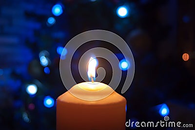 A burning orange candle on a dark background with blue lights - a Christmas New Year`s eve divination mystic esoteric romance lov Stock Photo