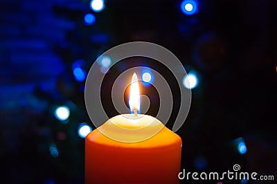 A burning orange candle on a dark background with blue lights - a Christmas New Year`s eve divination mystic esoteric romance lov Stock Photo