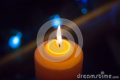 A burning orange candle on a dark background with blue lights - a Christmas New Year`s eve divination mystic esoteric Stock Photo