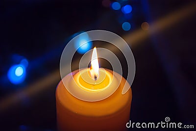 A burning orange candle on a dark background with blue lights - a Christmas New Year`s eve divination mystic esoteric Stock Photo