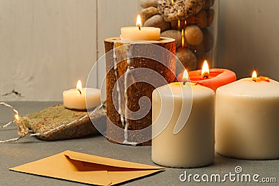 Burning thick white candles in wooden and stone candlesticks and a craft envelope on the table. close-up Stock Photo