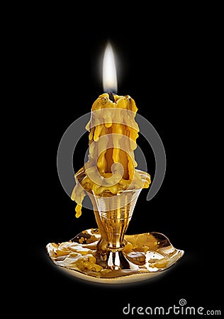 Burning vintage church candle wax in old gold candlestick close-up on a brilliant black mirror background. Stock Photo