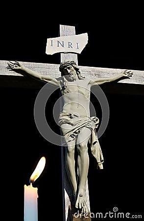 Lit candle shining in front of cement statue of Jesus Stock Photo