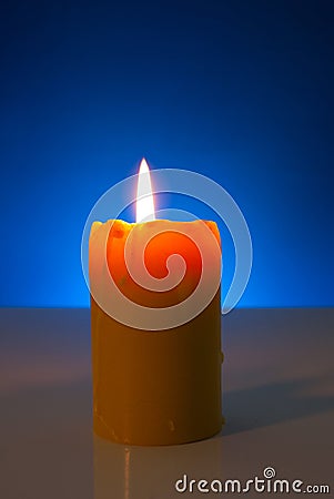 Burning yellow candle against blue background Stock Photo