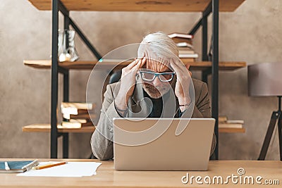 Burnout of people. Senior man holding his head at the workplace. Stress and problems at work, overwork. Irritating migraine Stock Photo