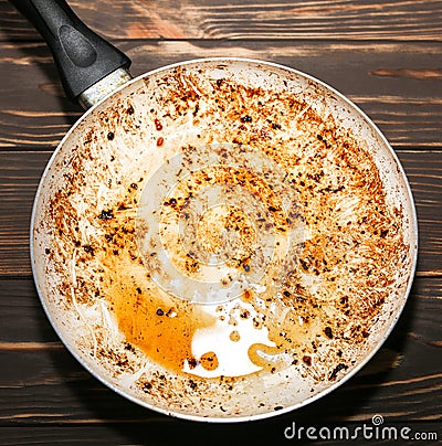 Burnt pan in oil. Damaged kitchenware. Wooden background. Unhealthy food Stock Photo