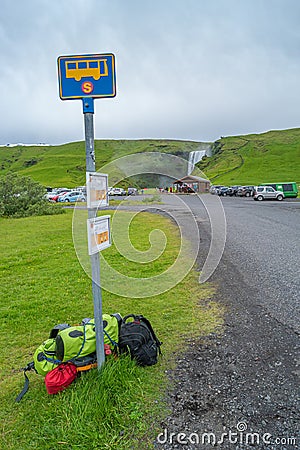 Bus stop and pile of backpacks at famous Skogafoss waterfall, while hiking in Iceland, summer, scenic dramatic view Editorial Stock Photo