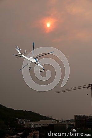 Bushfire sunset sky with an airborne helicopter in the foreground. Sun glow over Gosford city through wildfire smoke and haze. Stock Photo