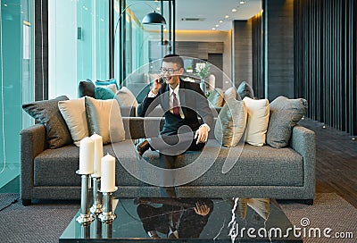 Business Asian man using a smartphone on sofa in luxury condo Stock Photo