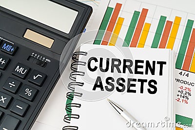 On business charts there is a calculator, a pen and a notepad with the inscription - CURRENT ASSETS Stock Photo