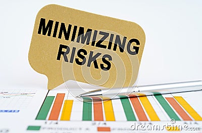 On the financial charts lies a pen and a sign with the inscription - MINIMIZING RISKS Stock Photo