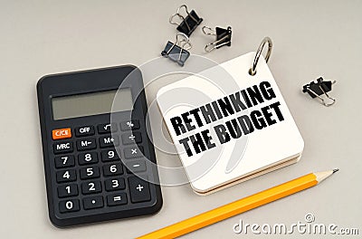 On a gray surface, a calculator, a pencil and a notepad with the inscription - Rethinking the budget Stock Photo